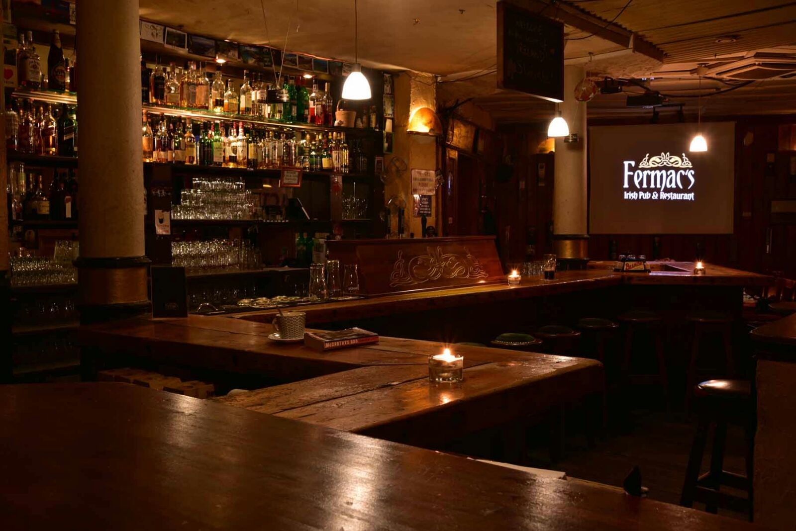 Die Bar im Fermac's – Kerzenlicht, Whiskey-Regal und das Logo auf der Leinwand